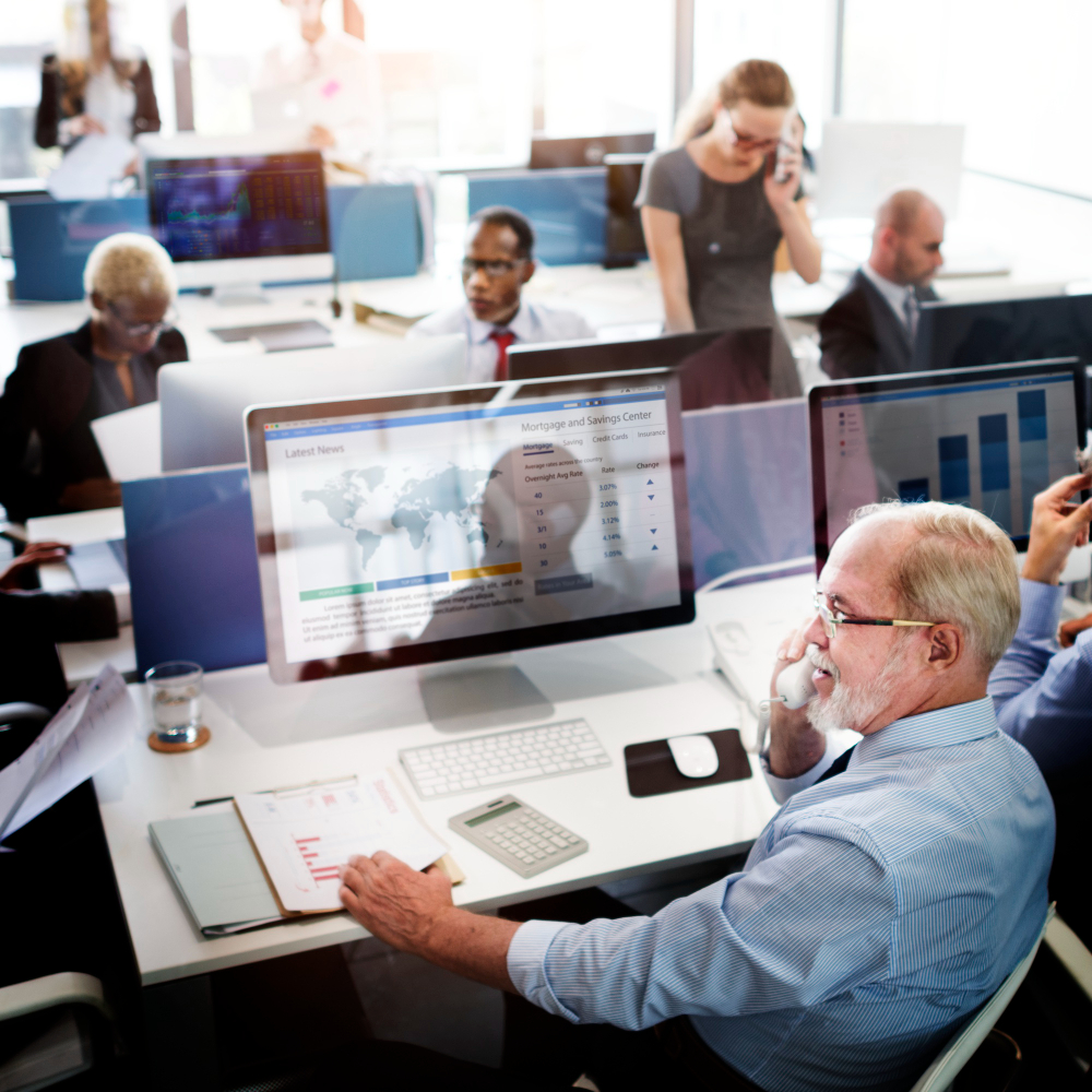A busy, open-concept office space where team members are working. Many of them are on phone calls with clients, overlooking spreadsheets and reports. 