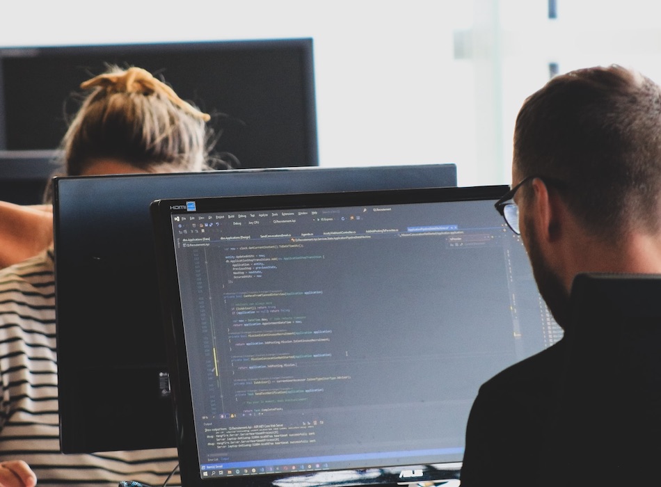 Two team members are focused on their computers at their shared desk. One of the team members is coding. 